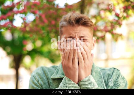 Junger Mann mit saisonaler Pollenallergie in der Nähe blühender Bäume am Frühlingstag Stockfoto