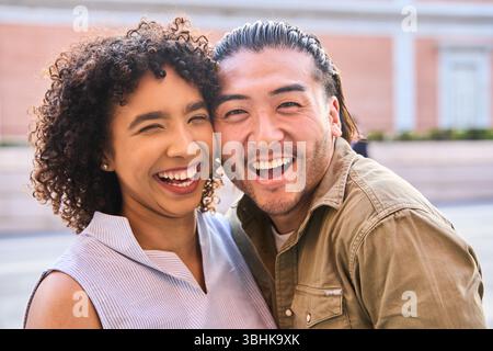 Das junge Multi-ethnische Paar lacht fröhlich und genießt die Gesellschaft des anderen in einer lebhaften städtischen Umgebung, die Glück und Liebe ausstrahlt Stockfoto