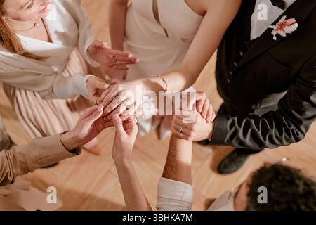 Gruppe junger erwachsener Männer und Frauen, die sich während der Hochzeitsfeier im Kreis mit Händen verbinden, zeigen Nahaufnahme der Hände mit Eheringen und formeller Kleidung, die Einheit symbolisieren Stockfoto