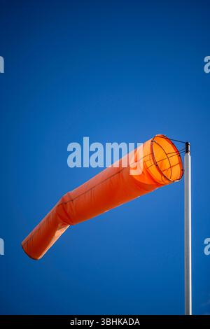 Eine hellorange Windsocke vor einem klaren blauen Himmel Stockfoto