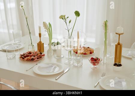 Hochzeitsfeierungstisch mit leeren Tellern, Kristallgläsern, goldenen Kerzenleuchtern, verschiedenen Vorspeisen und Desserts für Gäste Stockfoto