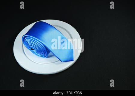 Eine blaue Krawatte rollte auf schwarzem Hintergrund mit Kopierraum Stockfoto