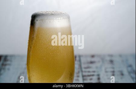 Eine Nahaufnahme eines mit goldenem Bier gefüllten Glases, das seinen schaumigen Kopf und die Kondensation auf dem Glas zeigt Stockfoto