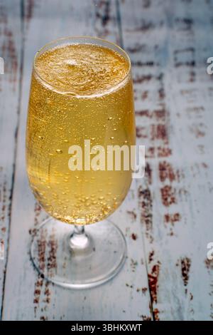 Eine Nahaufnahme von goldenem Bier in Stängelglas mit zahlreichen kleinen Blasen, die auf einem strukturierten Hintergrund an die Oberfläche steigen. Konzept des Feierns Stockfoto