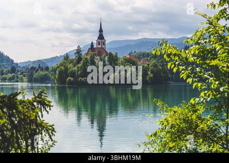 Ein traumhafter Blick auf den Bleder See in Slowenien mit blühenden Kastanienbäumen, die die Inselkirche vor den üppigen Hügeln der Alpen umrahmen. Hochwertige Fotos Stockfoto