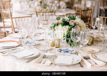 Schön gestalteter Esstisch mit feinem porzellan, Gläsern und einem üppigen Blumenaufsatz für Gäste. Stockfoto
