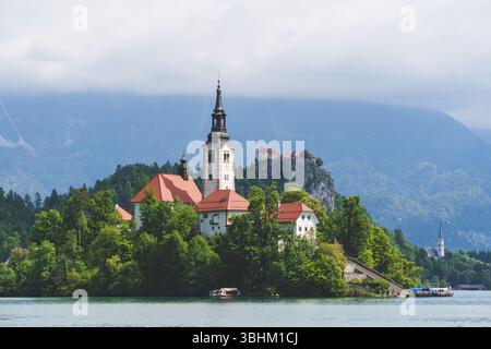 Ein traumhafter Blick auf den Bleder See in Slowenien mit blühenden Kastanienbäumen, die die Inselkirche vor den üppigen Hügeln der Alpen umrahmen. Hochwertige Fotos Stockfoto