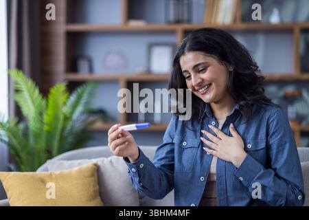 Eine glückliche Frau, die sich einen positiven Schwangerschaftstest ansieht, begeistert von den Nachrichten, Indoor-shot. Stockfoto
