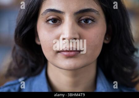 Nahaufnahme Porträt einer jungen brünetten Indianerin in einem blauen Hemd drinnen, die ernsthaft in die Kamera schaut. Stockfoto