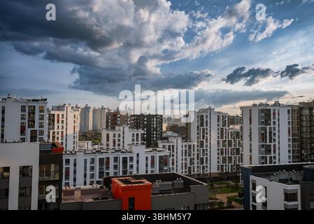 Zeitgenössischer Wohnkomplex mit hohen Apartmenthäusern vor einem dramatischen, wolkenreichen Himmel. Die Szene fängt urbanes Leben mit architektonischer Symmetrie und lebhaften Farben ein Stockfoto