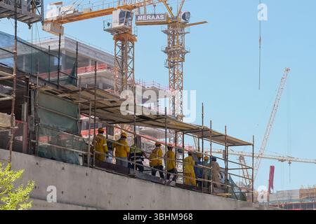 Gruppe von Bauarbeitern, die Sicherheitskleidung tragen, während sie auf Gerüsten laufen, um für die Tagesschicht zu wechseln. Stockfoto