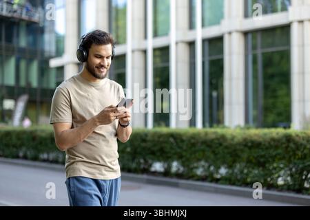 Ein junger Mann genießt seinen Lauf, während er Musik auf seinen Kopfhörern hört, sein Smartphone überprüft und lächelt. Stockfoto