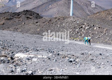Catania, Sizilien - Italien - 22.04.2025: Zwei Wanderer mit Rucksäcken und Trekkingstöcken wandern auf einem zerklüfteten Vulkanweg auf dem Ätna, umgeben von R Stockfoto