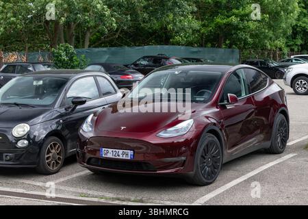 Nancy, Frankreich - Blick auf ein burgunderrotes Tesla Model Y, das auf einem Parkplatz mit anderen Autos geparkt ist. Stockfoto