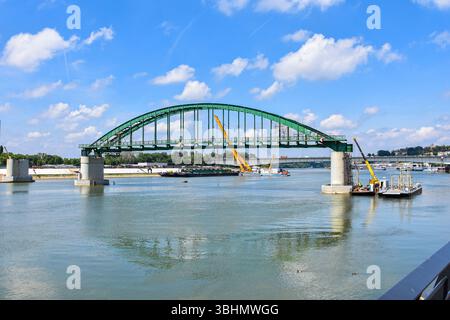 Mächtige Maschinen und Teams demontieren die legendäre Save Bridge, eingerahmt von Kalemegdan Festung, blauem Himmel und ruhigen Flussreflexen. Stockfoto