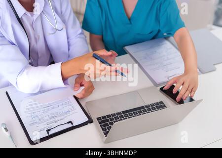 Asiatische Erwachsene Ärzte arbeiten an der Patientenversorgung zusammen und prüfen Dokumente auf einem Laptop an ihrem Schreibtisch diskutieren sie Gesundheitsinformationen Behandlung p Stockfoto