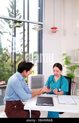 Eine asiatische Erwachsene Ärztin, die Peelings trägt, benutzt einen Stift, um das Handgelenk und die Hände eines erwachsenen männlichen Patienten während einer medizinischen Konsultation in einer Klinik zu untersuchen. T Stockfoto