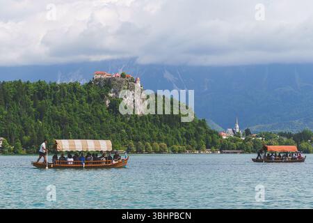 Traditionelle Pletna-Boote mit Touristen auf dem Bleder See, Slowenien, mit Schloss Bled sichtbar auf der Klippe. Hochwertige Fotos Stockfoto