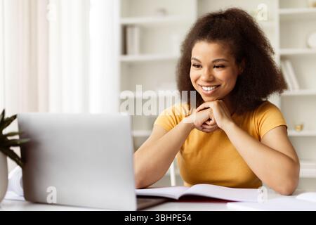Lächelnde Junge Schwarze Frau, Die Zu Hause Ein Notebook Zum Studium Oder Zur Arbeit Verwendet Stockfoto