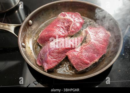 Frisches rohes Rindfleisch wird in heißem Öl mit viel Dampf in einer Karbonstahl-Pfanne gebraten, Fleisch kochen, ausgewählten Fokus, enge Schärfentiefe Stockfoto