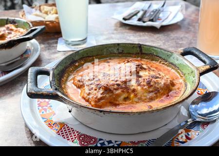 Lasagne, italienische Pasta mit Hackfleisch, Tomatensauce und Mozzarella in einem rustikalen Keramikauflauf auf einem Esstisch in einem Restaurant, ausgewählt für Fo Stockfoto