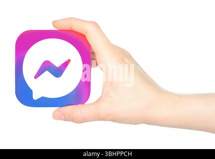 Die Hand hält das Symbol der mobilen Facebook Messenger App auf Papier auf einem transparenten Hintergrund. Facebook Messenger ist eine firmeneigene Instant Messaging-App in den USA Stockfoto