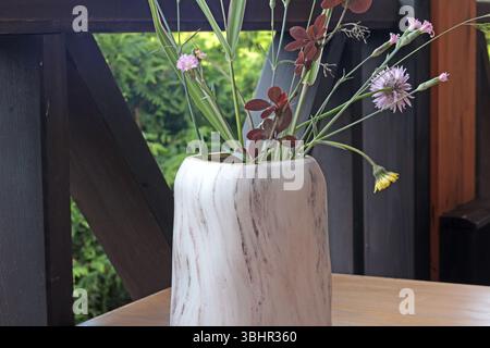 Marmorvase mit Wildblumen auf dem Tisch. Terrasse im Sommer. Design und Holzmöbel. Stockfoto