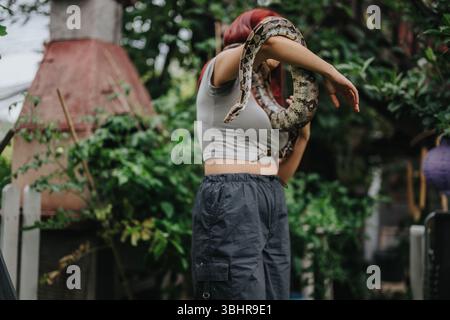 Mädchen im Garten, das draußen eine große Schlange auf der Schulter hält Stockfoto