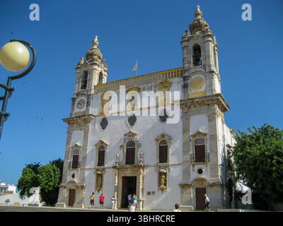 Ein wunderschöner Blick auf die Carmo-Kirche in Faro, Portugal, mit ein paar Leuten in der Nähe des Eingangs. Stockfoto