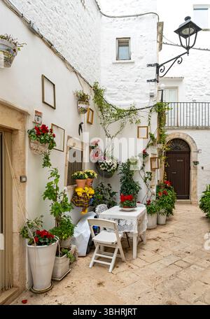Enge Straße mit Tisch und Stühlen in der weißen Stadt Locorotondo, Apulien - Apulien, Italien Stockfoto