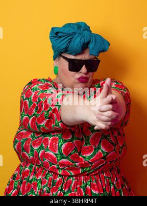 Eine lustige Frau in Übergröße, die eine Fingerpistole in einer Sonnenbrille macht Stockfoto