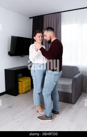 Ein Paar tanzt fröhlich in einem stilvollen Wohnzimmer, eingetaucht in ihren gemeinsamen Moment, mit einem sanften Lächeln, das ihre Gesichter beleuchtet, und einem charmanten atmos Stockfoto