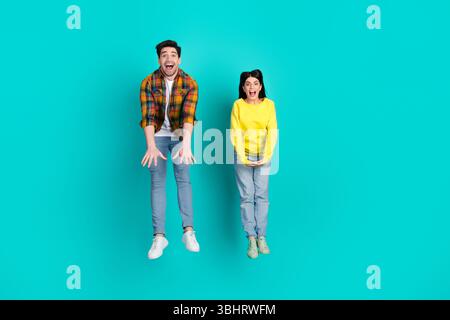 Glückliches junges Paar, das vor Freude in stylischen, legeren Outfits vor leuchtendem blauem Hintergrund springt Stockfoto