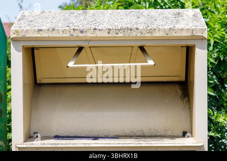 Eine Nahaufnahme eines verwitterten, hellen Metallspendenbehälters mit strukturiertem Dach. Grünes Laub ist im Hintergrund sichtbar. Stockfoto