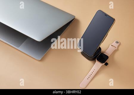 Laptop mit Smart Watch und Smartphone-Aufladung über kabelloses Ladegerät auf beigefarbenem Tisch, modernes Arbeitsplatzgerät Stockfoto