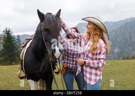 Lächelndes Mädchen, das sich mit einem Pferd verbindet, lernt die Grundlagen des westlichen Reitens mit einem Cowgirl-Lehrer in einer atemberaubenden natürlichen Umgebung Stockfoto