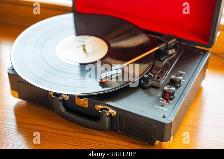 Vintage-Plattenspieler im Koffer-Stil, der Vinyl-Schallplatte dreht. Retro-Musik in Bewegung schafft nostalgische Atmosphäre im Innenraum Stockfoto