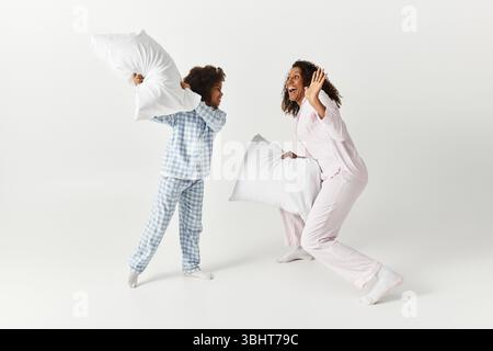 Schwarze Mom und ihre Tochter genießen Kissenkampf, beide sind in passenden PJs. Stockfoto