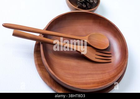 Rustikale Holzschale mit passendem Löffel und Gabel auf einer hellen Oberfläche, die natürliche, umweltfreundliche Speisen präsentiert. Perfekt für Lebensmittelfotografie, Stockfoto