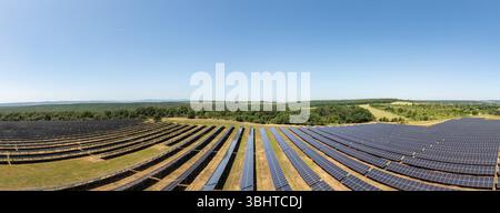 Aus der Vogelperspektive eines großen Solarkraftwerks mit Reihen von Photovoltaikpaneelen, die auf freiem Land installiert sind und unter klarem Himmel saubere erneuerbare Energie erzeugen Stockfoto