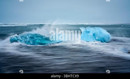 Diamantstrand in Island, mit Cyan-Eisbergen, die im Meer schwimmen und die Wellen in Bewegung sind. Stockfoto
