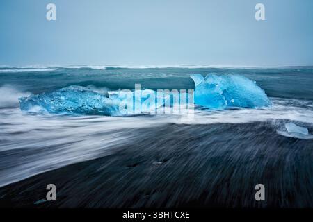 Diamantstrand in Island, mit Cyan-Eisbergen, die im Meer schwimmen und die Wellen in Bewegung sind. Stockfoto