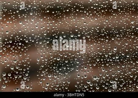 Monochrome Textur von Regentropfen auf Fensterglas gegen Stadtgebäude. Nahaufnahme Stockfoto