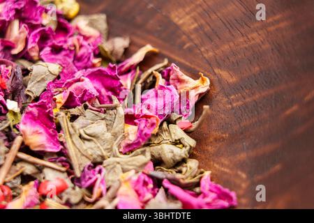 Trinken Sie Zutaten mit getrockneten grünen Teeblättern und Rosenblättern in einer Holzschale Stockfoto