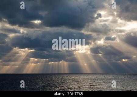 Die Sonnenstrahlen bahnen ihren Weg durch den bewölkten Himmel im offenen Meer. Stockfoto