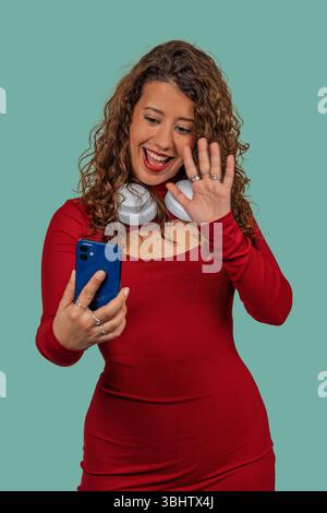 Glückliche junge Frau mit Kopfhörern, die während eines Videoanrufs zu ihrem Smartphone winkt Stockfoto