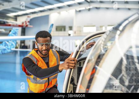 Flugzeugwartungsingenieur trägt eine Schutzbrille und eine Warnweste und führt eine Inspektion vor dem Flug an einem kleinen Flugzeug in einem Luftstrom durch Stockfoto