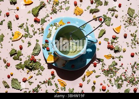 Teetasse mit Metall-Infuser, Teeblättern, getrockneten Beeren und Orangenscheiben verstreut auf rosa Hintergrund. Gesundes Getränk und entspannendes Ritual. Stockfoto