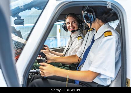 Zwei lächelnde Piloten in Kopfhörern und Uniformen sitzen im Cockpit eines kleinen Flugzeugs, bedienen die Steuerung und kommunizieren Stockfoto