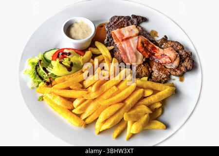 Zwei Steaks mit gebratenem Speck, Pommes frites, Gemüse und Salat, Sauce. Alles auf weißem Teller, Nahaufnahme. Stockfoto